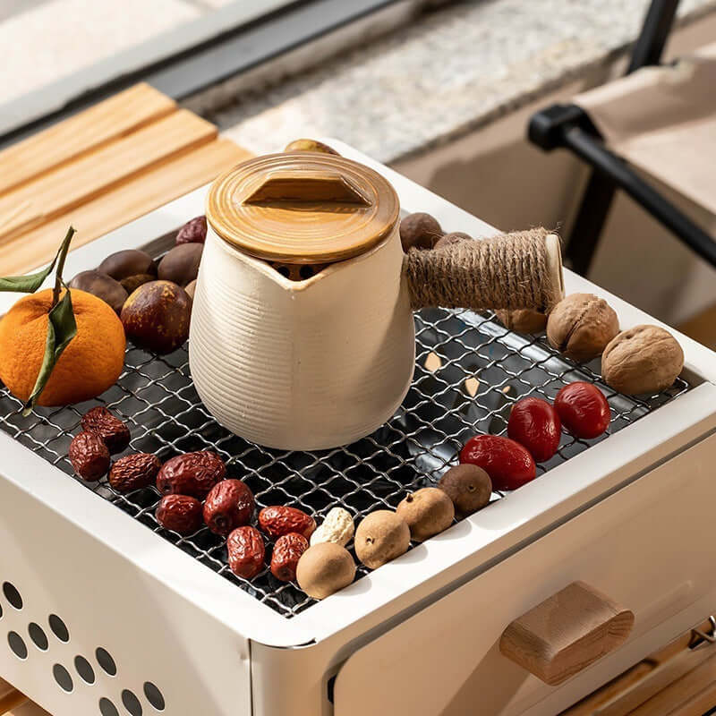 Outdoor barbecue oven with a kettle and assorted fruits on the grill net, showcasing a cozy grilling setup.
